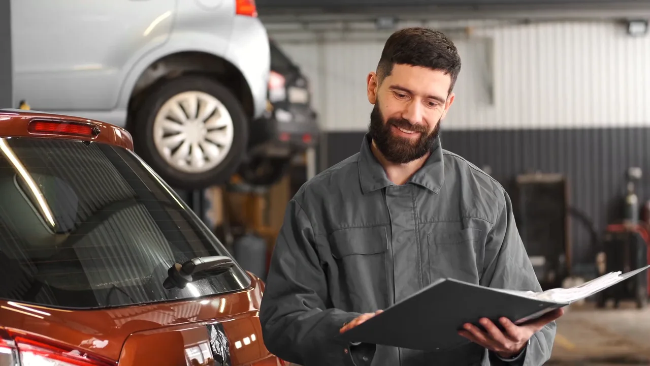 Mechanic reviewing a job folder beside a car in a repair shop